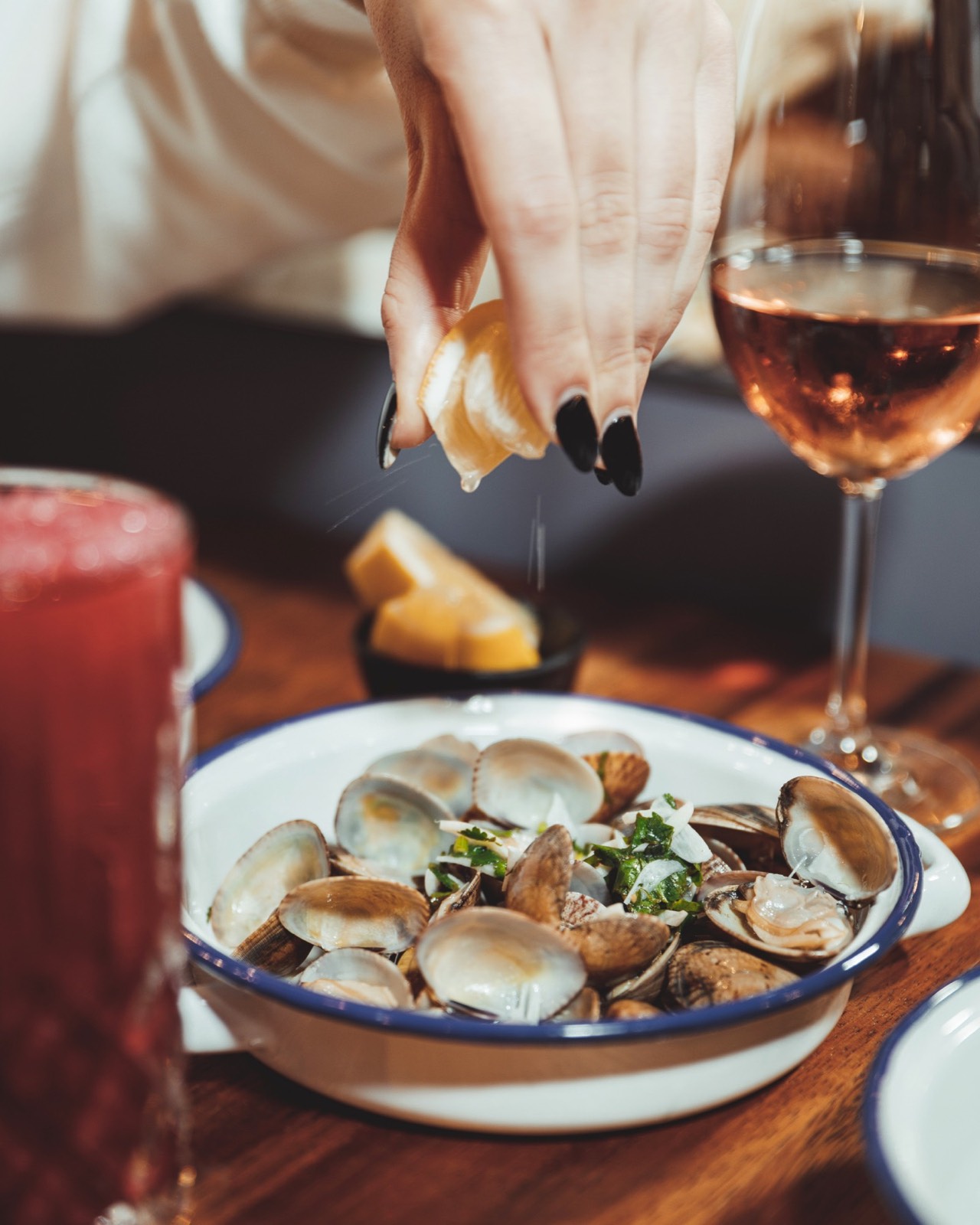 Amêijoas com limão espremido à mesa, ao lado de um copo de rosé